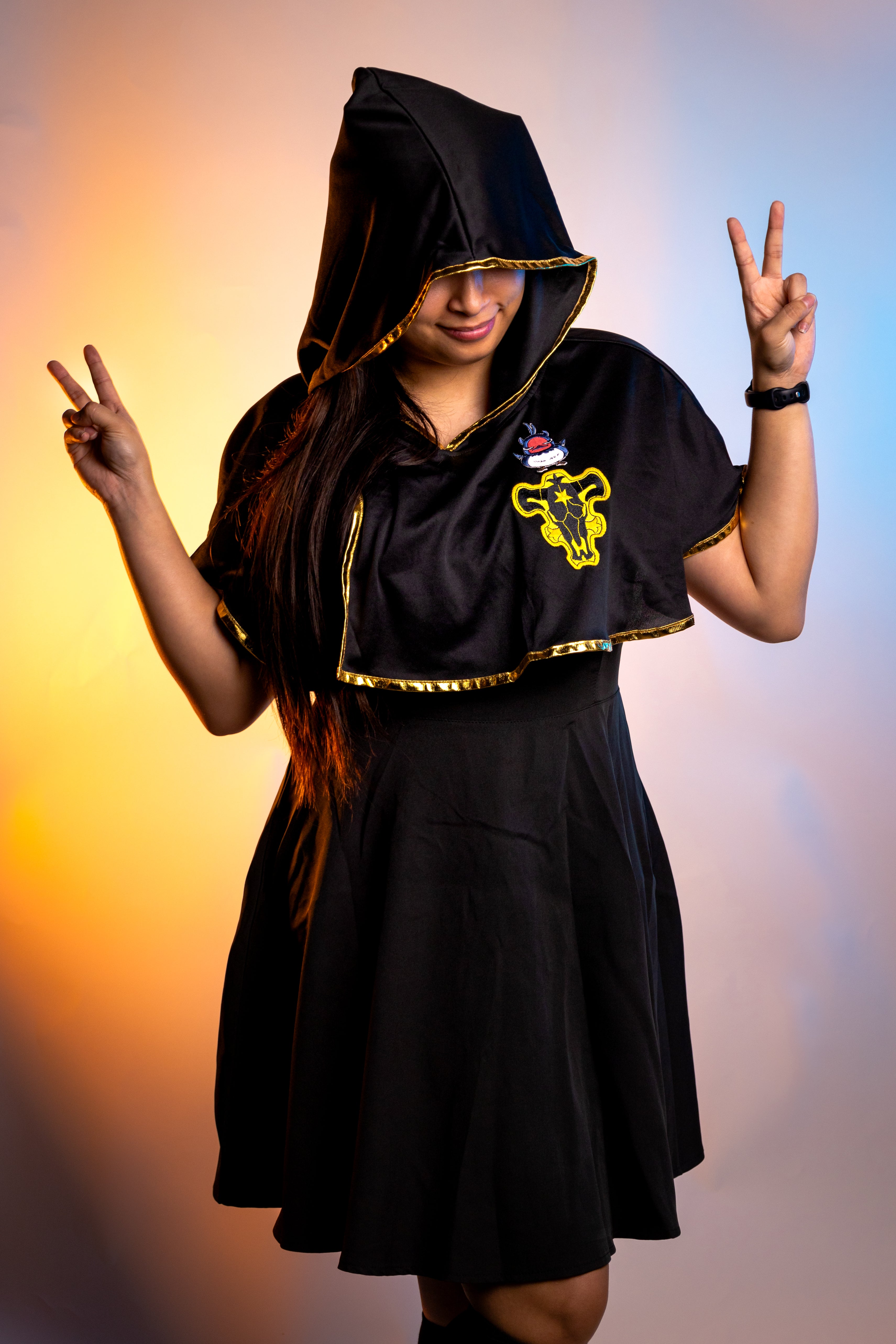 Person wearing a black hooded outfit with a yellow logo against a gradient background