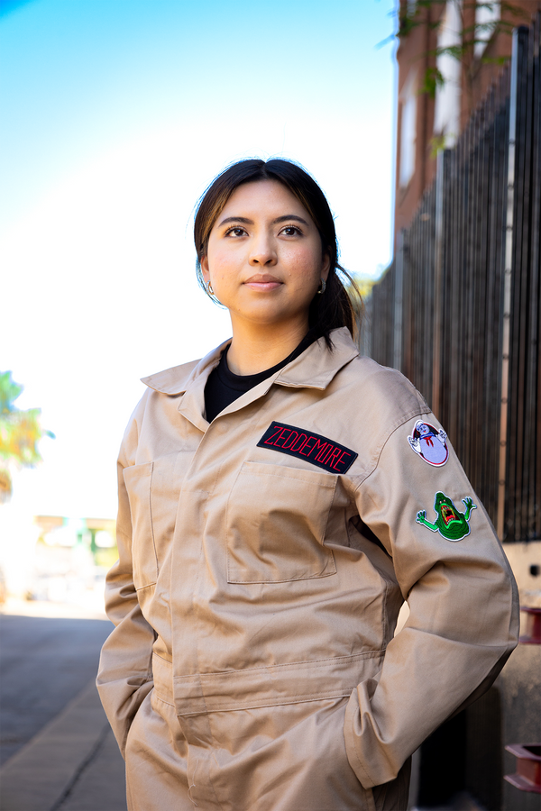 Person wearing a beige jumpsuit with patches in an outdoor setting